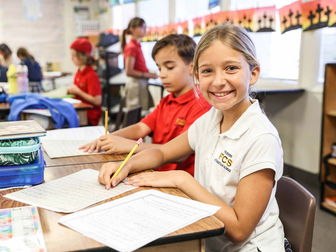 Smiling elementary student in uniform writing at her desk in class