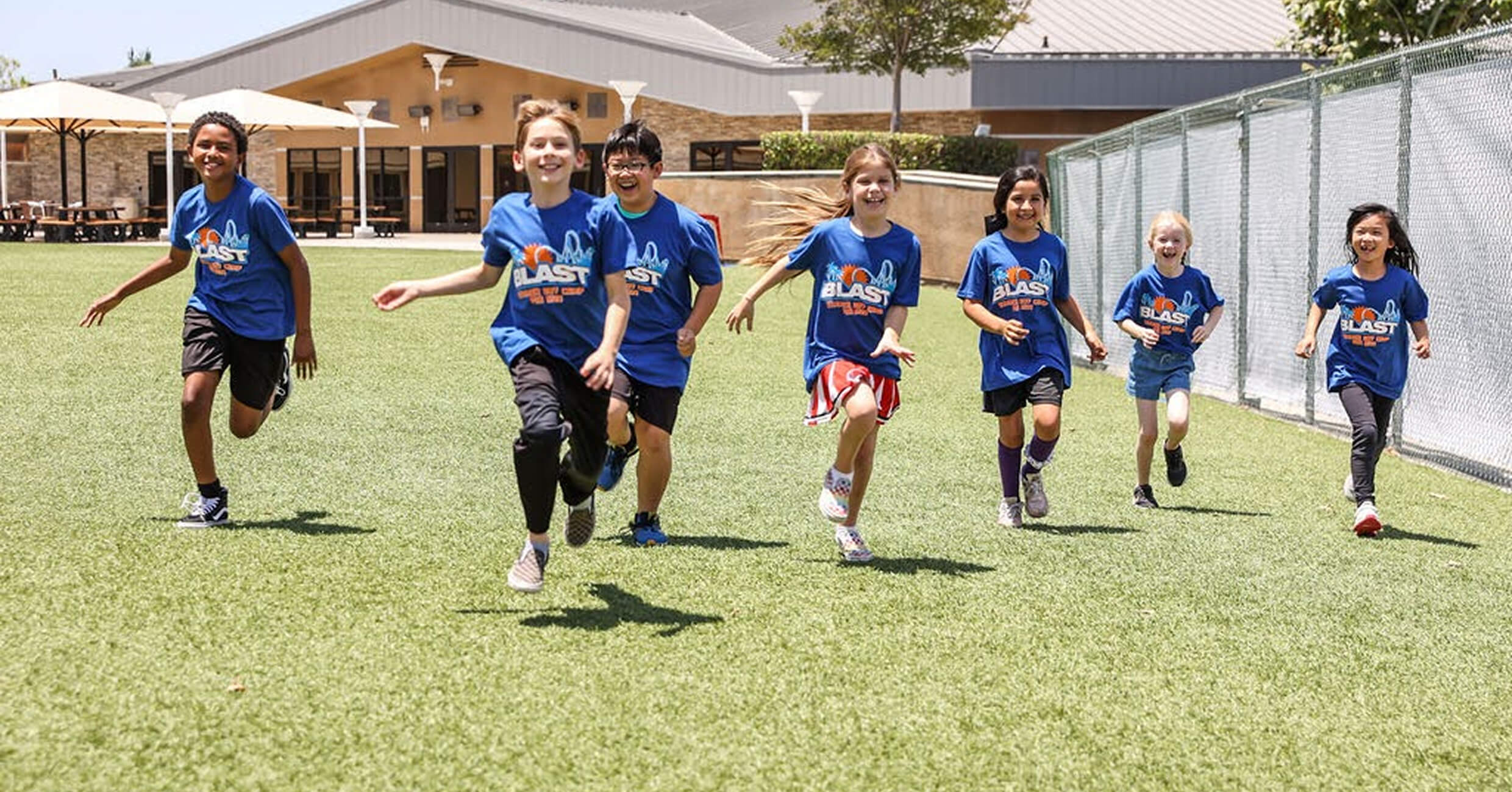 Students in blue shirts running across the grass field on campus