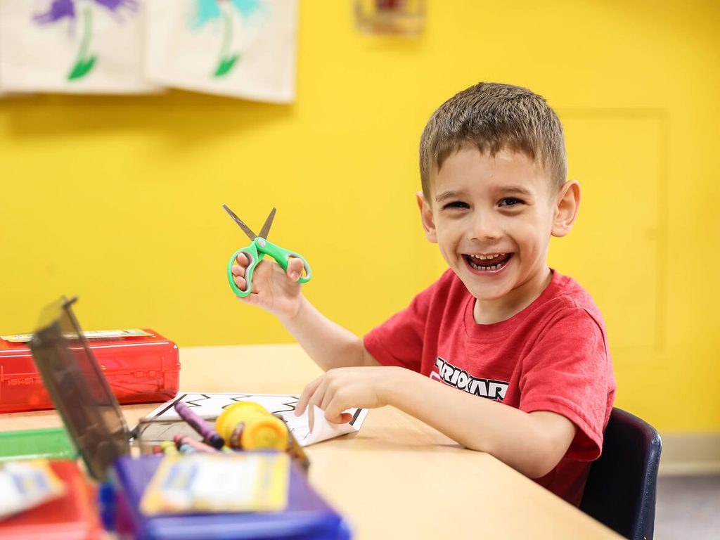 Smiling young boy cutting paper with scissors during an art activity
