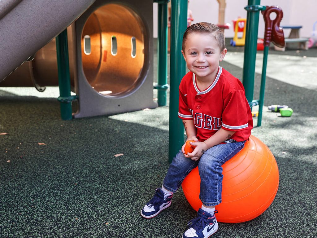 Smiling young boy bouncing on an orange ball on the playground