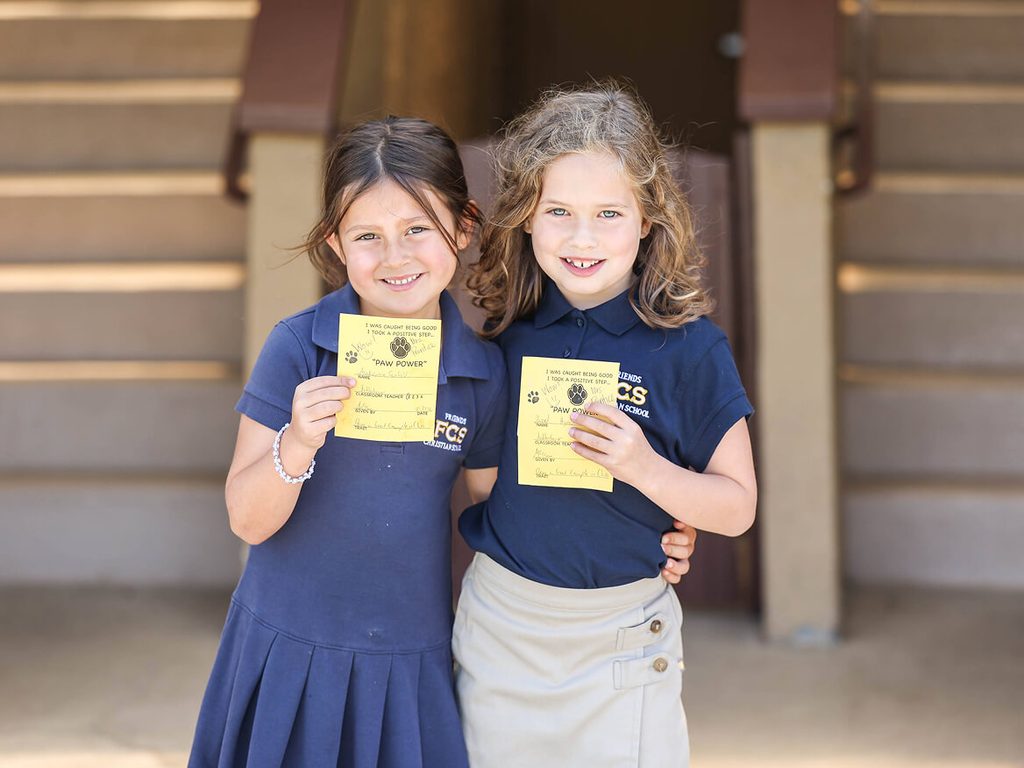 Two smiling girls in school uniforms holding yellow cards
