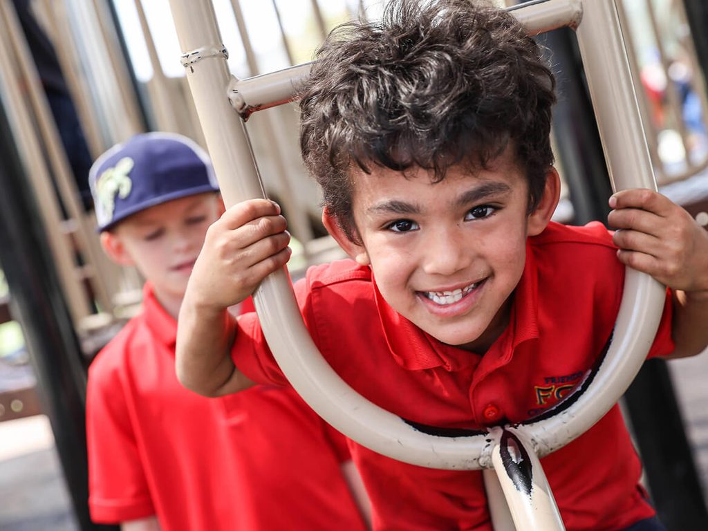 Smiling boy in a red uniform shirt playing on the playground equipment