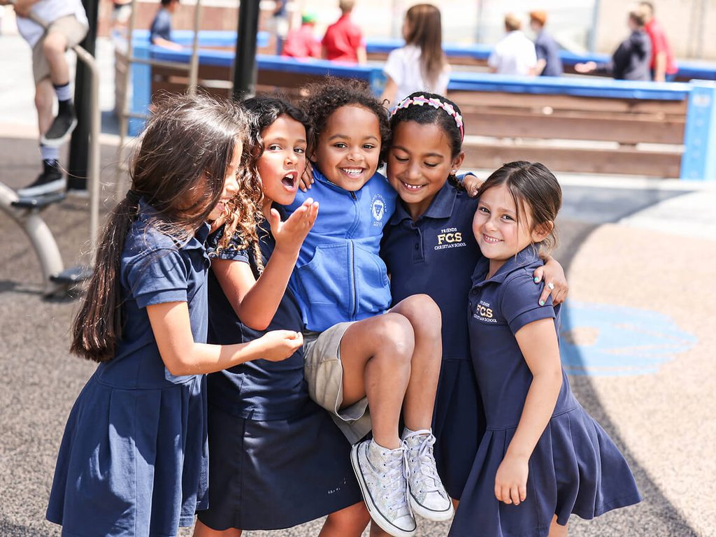 Group of smiling girls in school uniforms hugging on the playground
