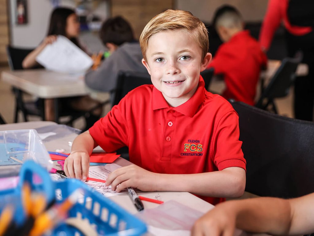 Smiling elementary boy in a red uniform shirt at his desk