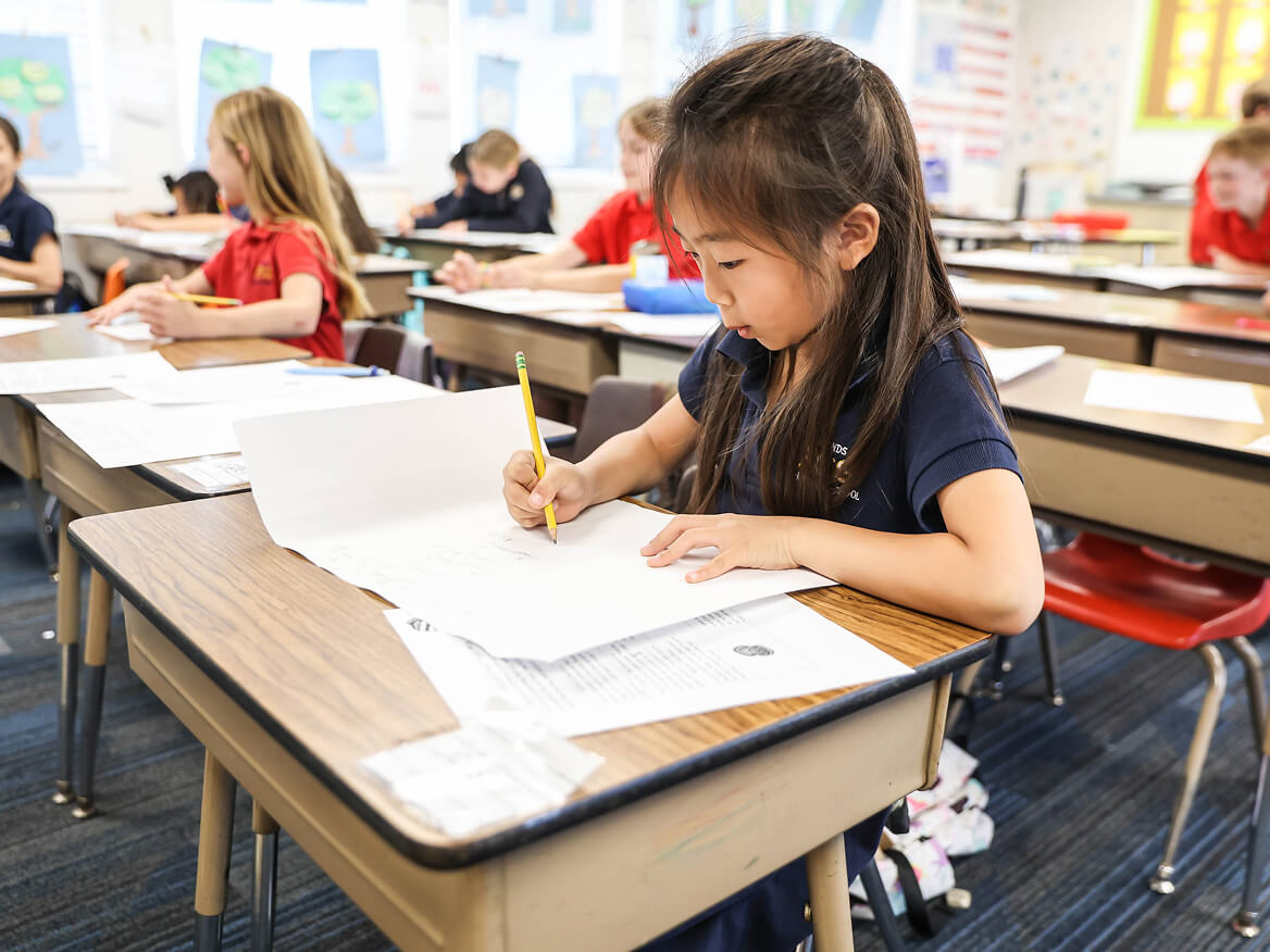 Students writing at their desks in a bright classroom