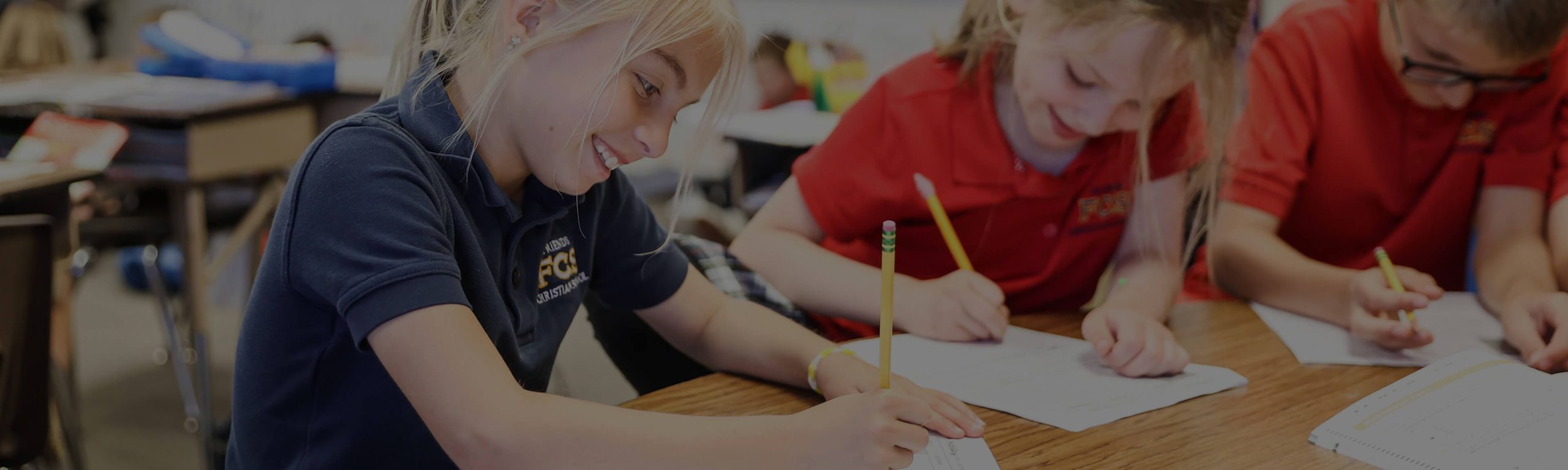 Elementary students writing on worksheets at a classroom table