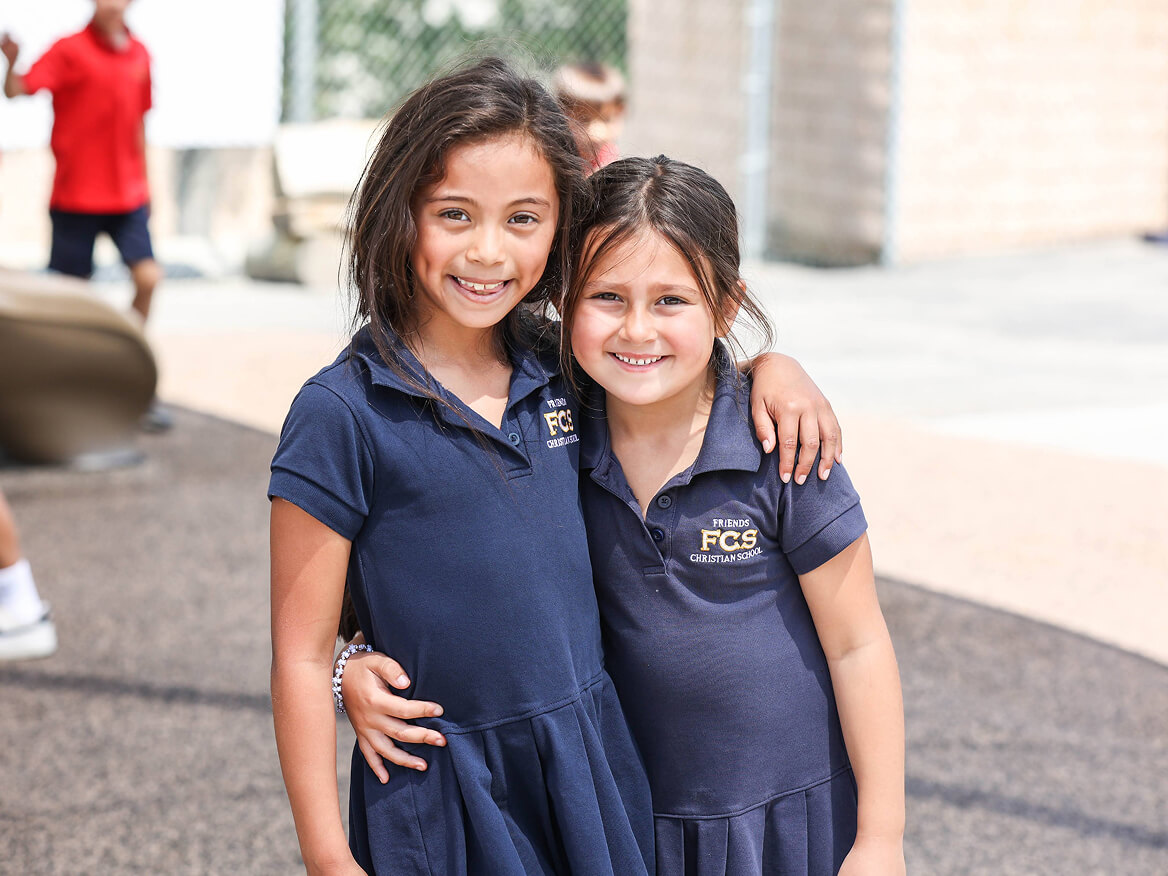Two smiling girls in navy school uniforms hugging on campus