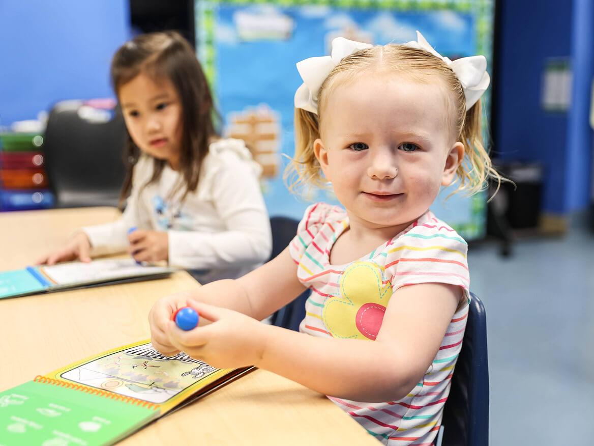 Smiling preschool girl playing at a classroom table