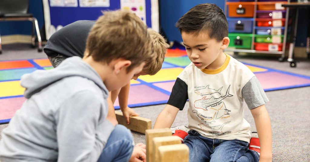 Two young boys building with wooden blocks on the classroom rug