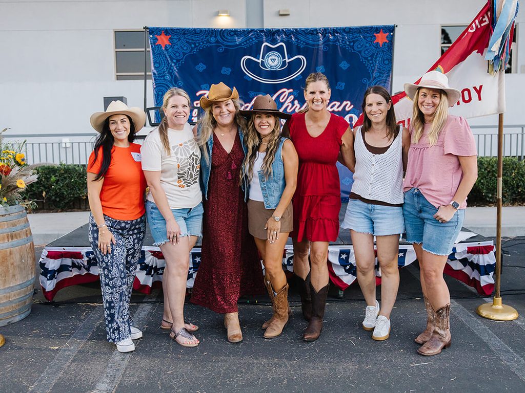 Group of moms in western outfits posing in front of a Friends Christian School banner