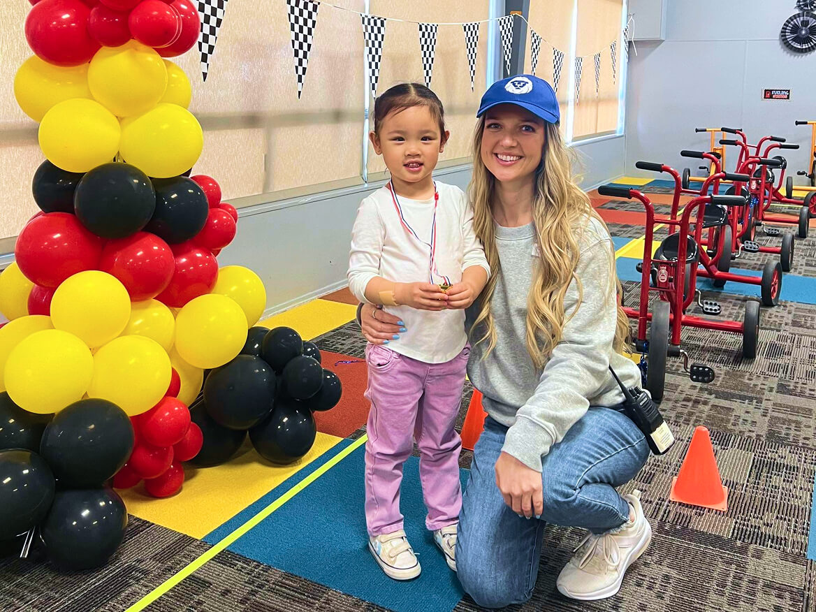 Young student and teacher posing next to a red, yellow and black balloon column
