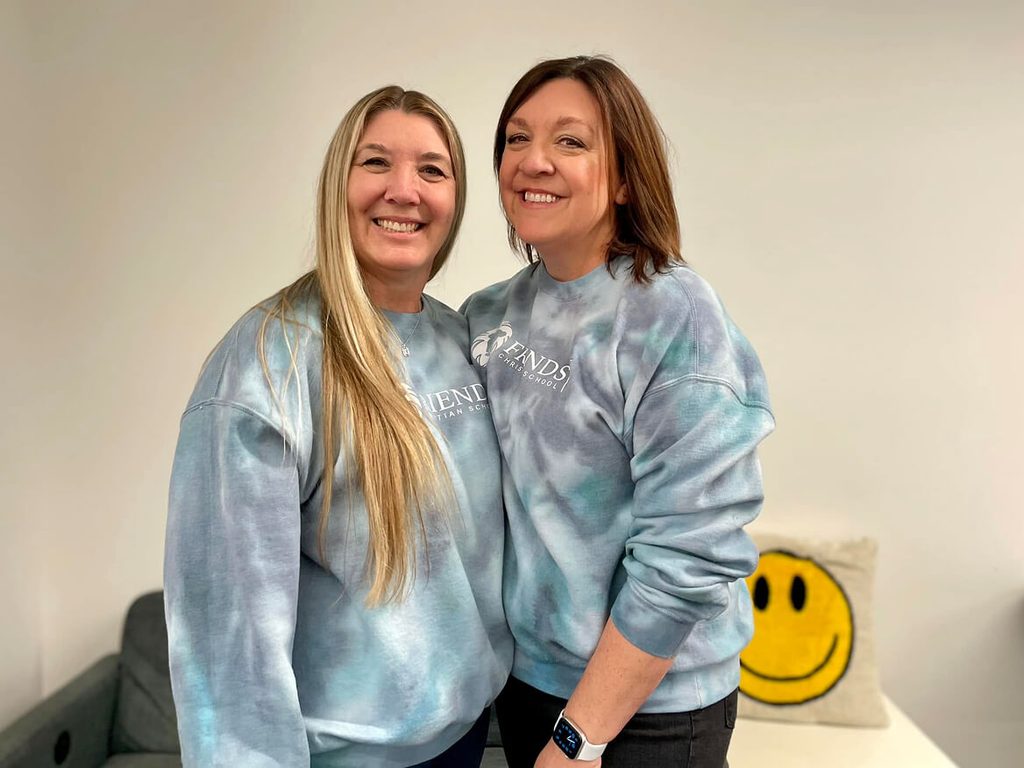 Two smiling women in matching tie-dye sweatshirts on campus