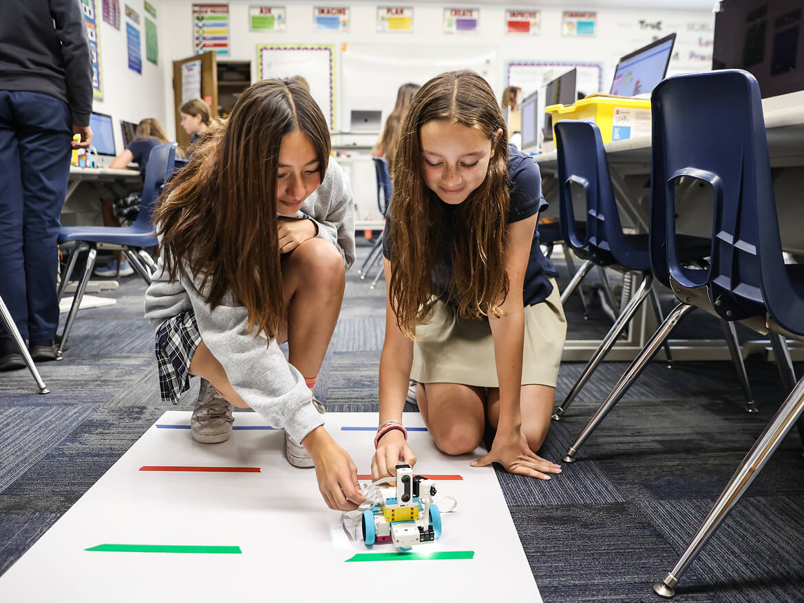 Two students kneeling on the classroom floor working on a robotics project