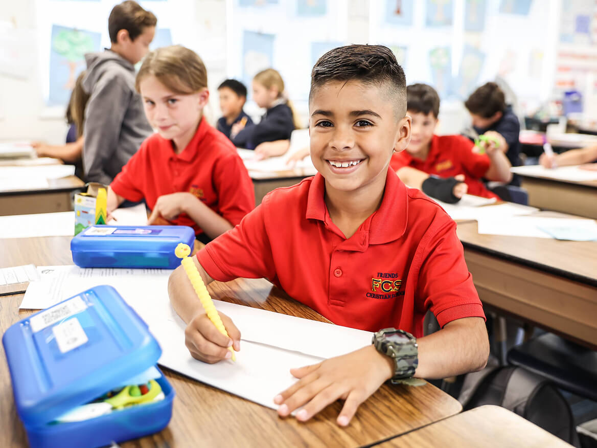 Smiling elementary boy in a red uniform shirt working at his desk
