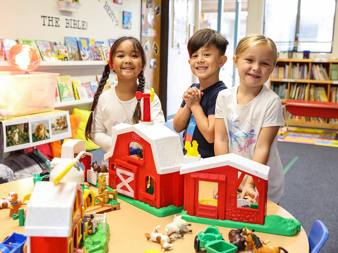 Smiling young students playing with a toy farm set in the classroom