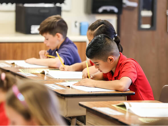 Elementary students writing at their desks during a classroom lesson