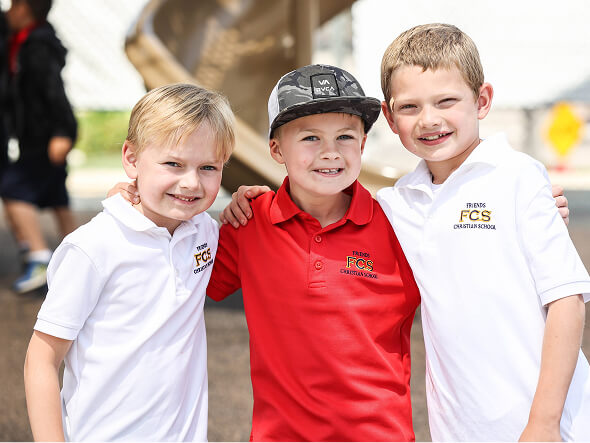 Three smiling kindergarten boys in school uniforms with their arms around each other
