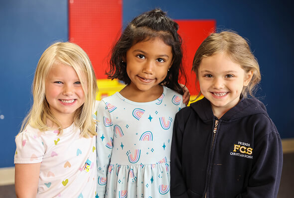 Three smiling young girls standing together in front of a colorful wall