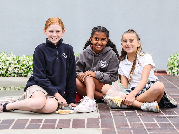 Three smiling middle school girls sitting together on the campus courtyard