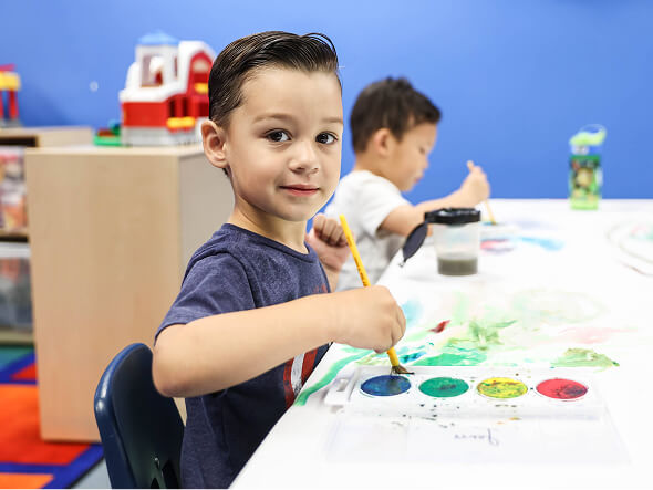 Smiling preschool boy painting with watercolors at a classroom table