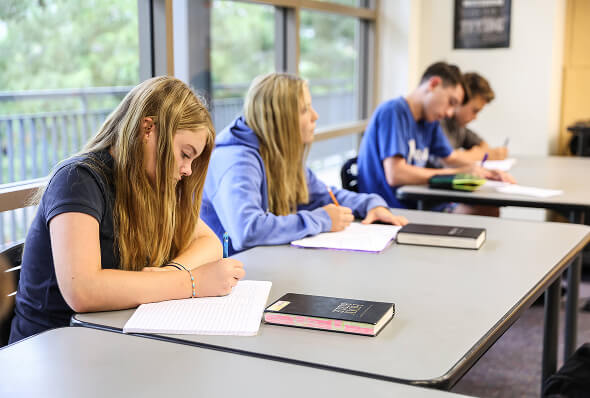 Middle school students reading their Bibles and taking notes in class