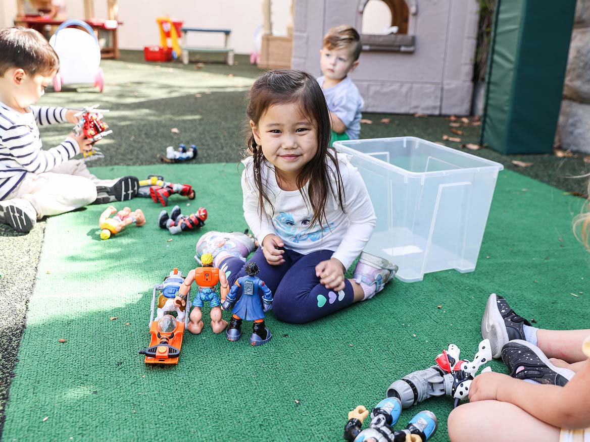 Young preschool girl smiling while playing with toys on the playground turf