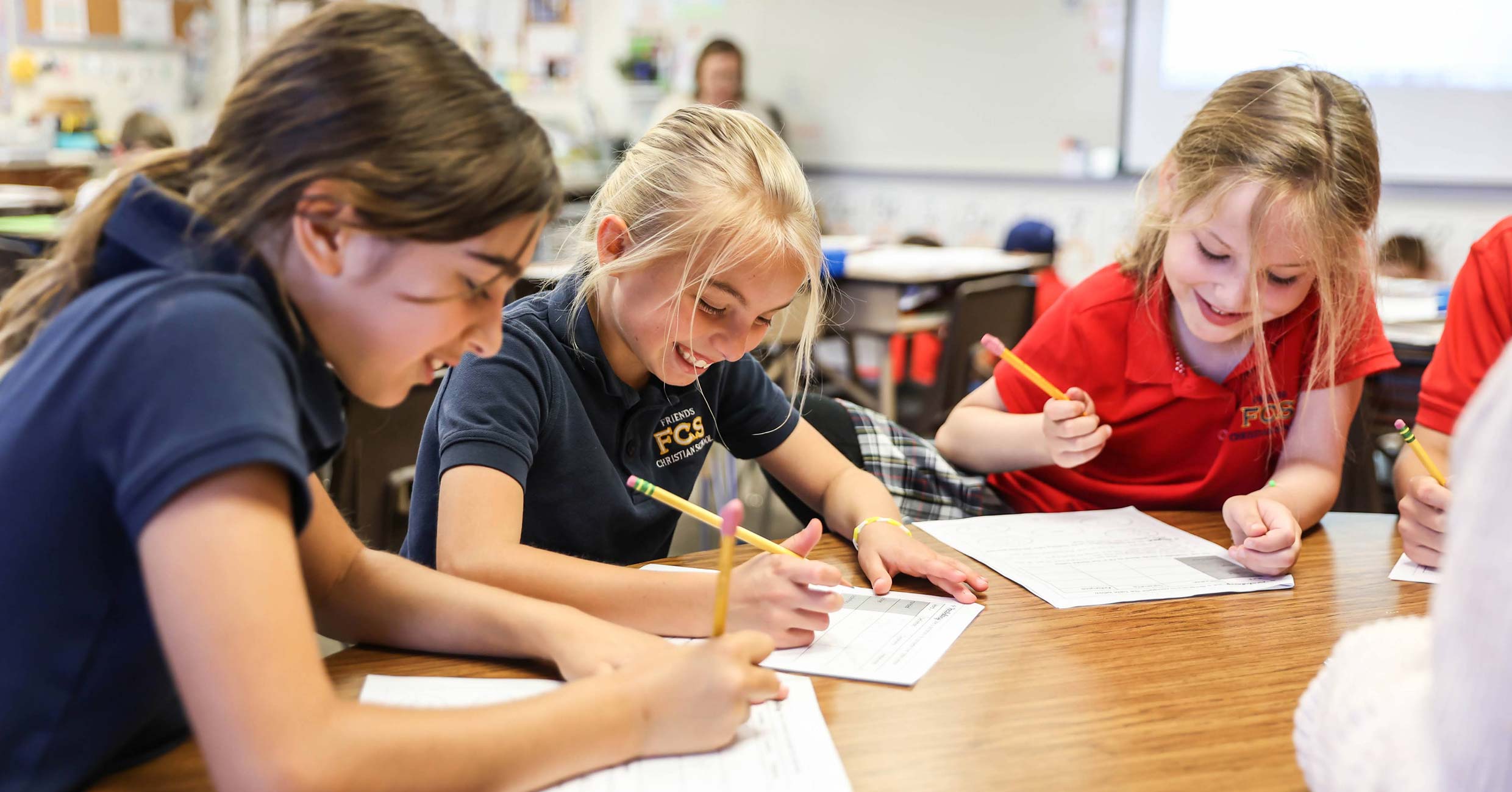 Elementary students in school uniforms working on worksheets together at a classroom table