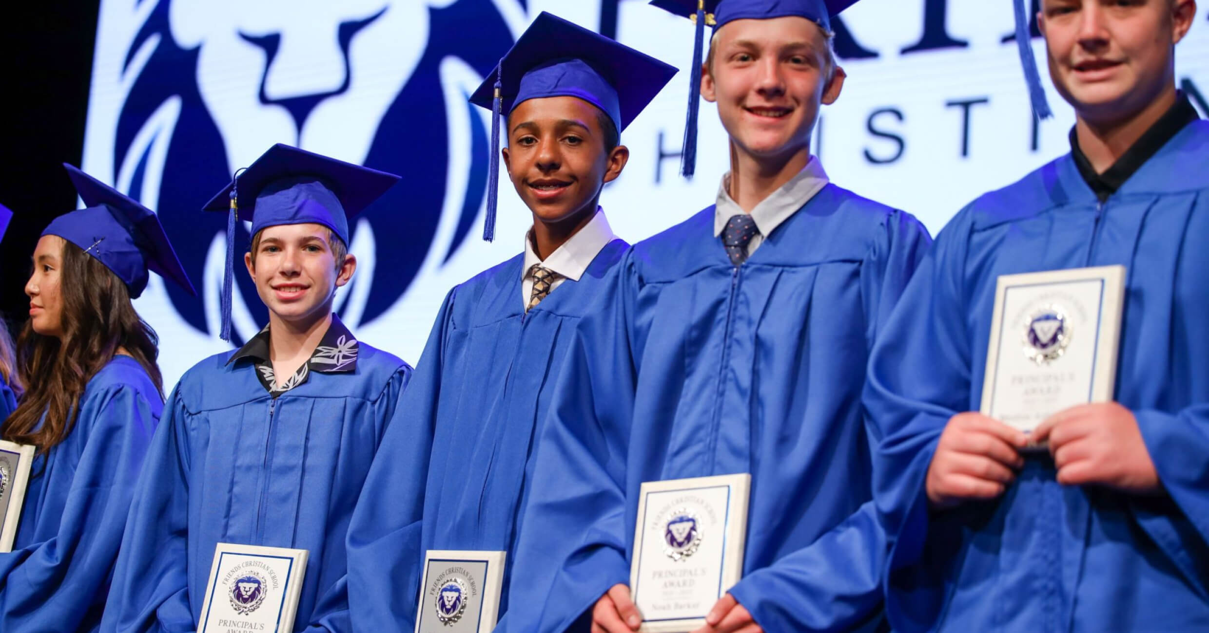 Friends Christian School graduates in blue caps and gowns holding their diplomas
