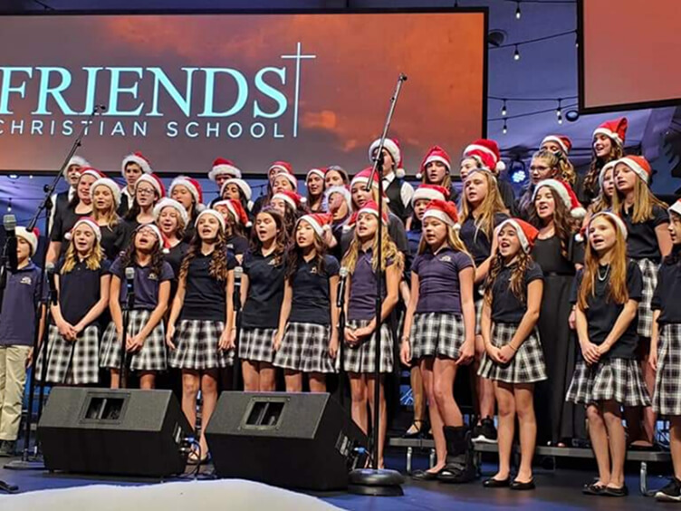 Friends Christian School choir in uniforms and Santa hats singing at a Christmas concert