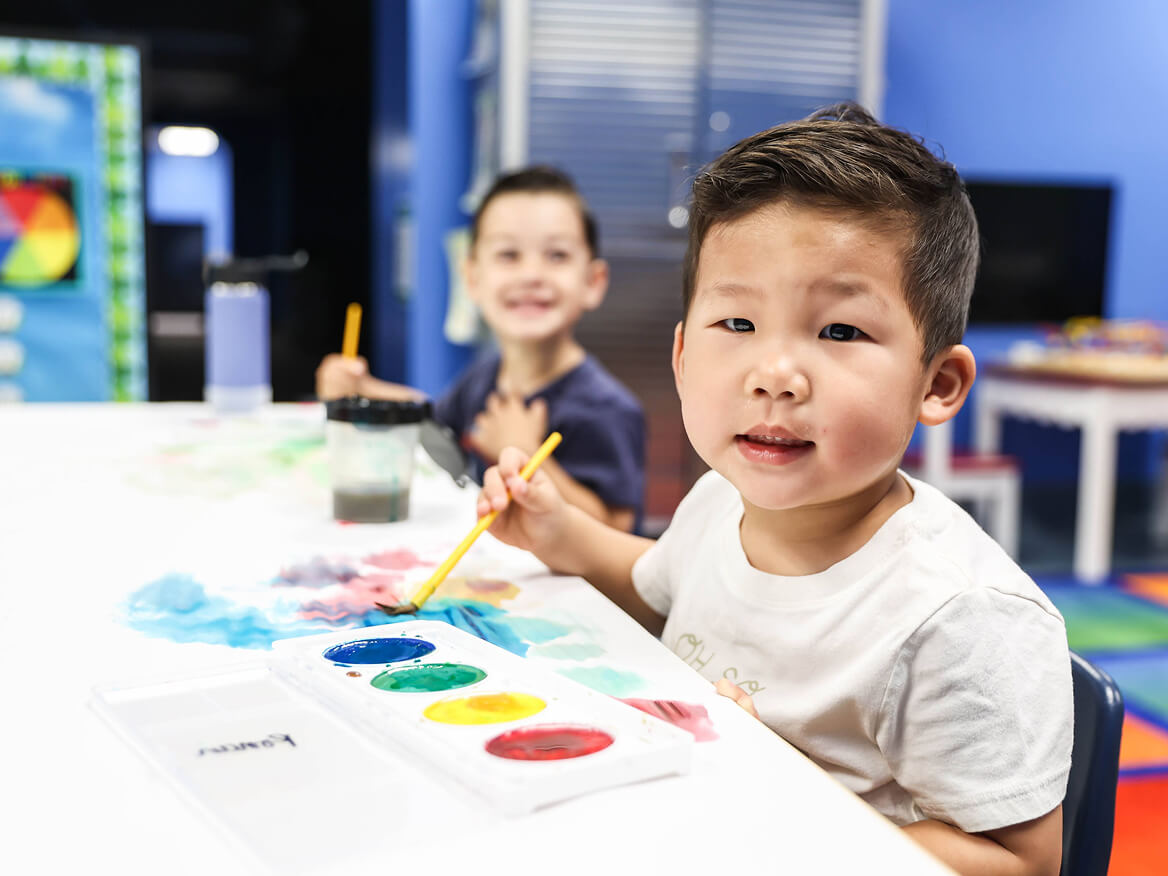 Smiling young boy painting with watercolors at a classroom table