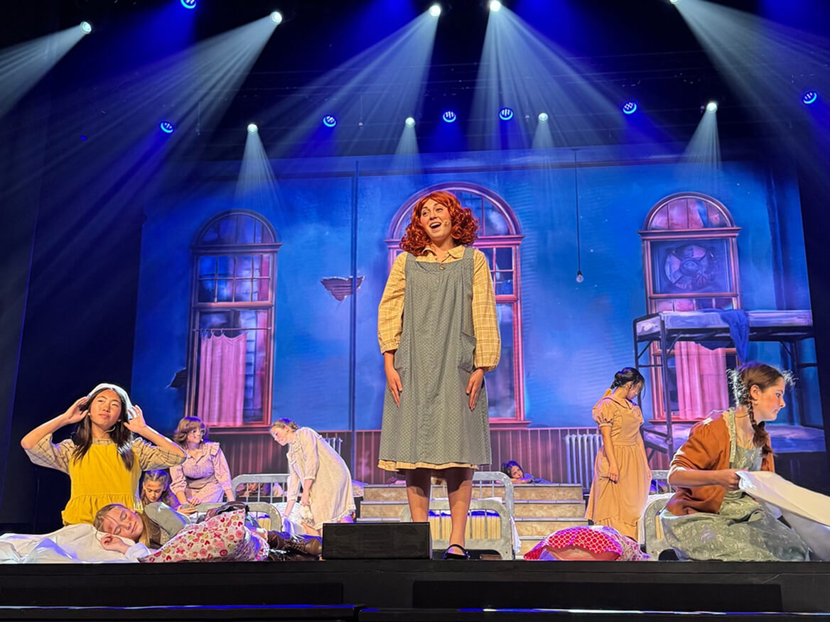 Student actors performing a scene from a musical under blue stage lights