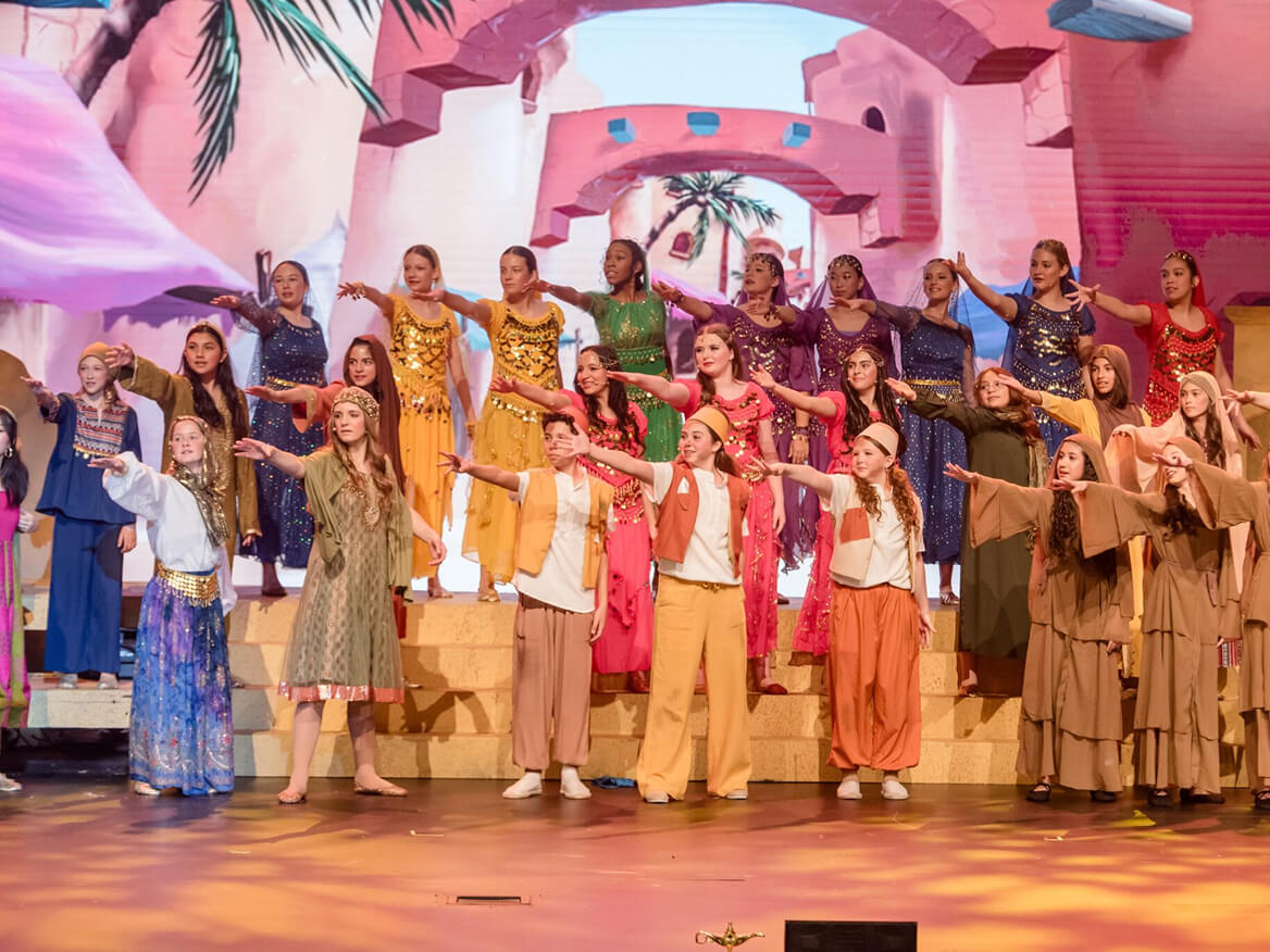 Students in colorful costumes performing a musical number on a desert-themed stage