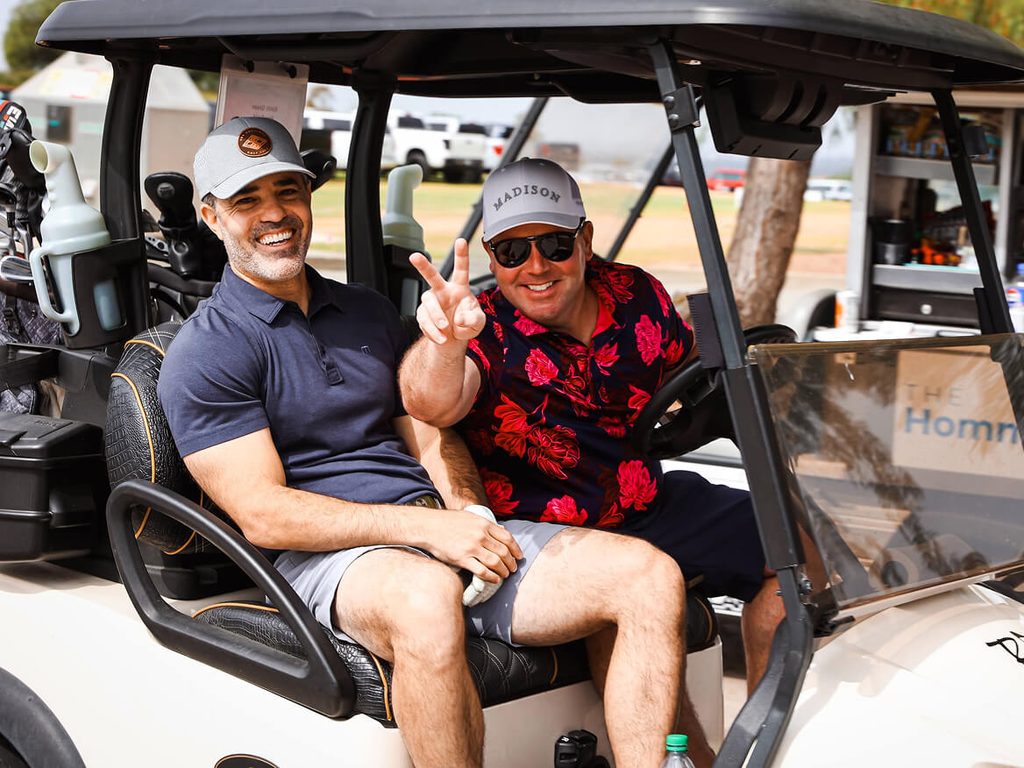 Two men smiling in a golf cart at the school golf tournament